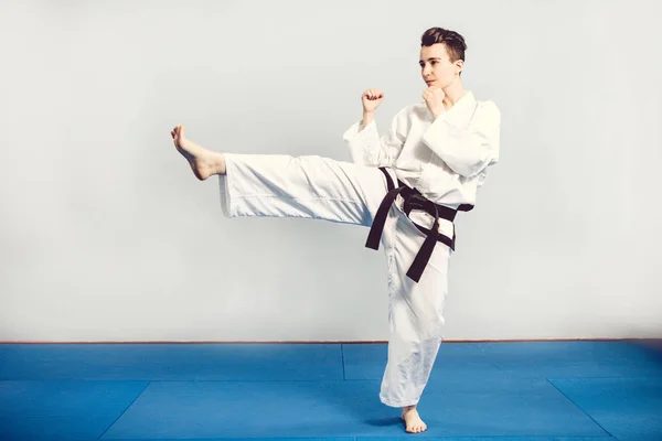 Chica en traje de karate kimono en estudio en fondo gris. Niña muestra judo o karate stans en uniforme blanco con negro. Deporte individual de arte marcial. Retrato de cuerpo completo — Foto de Stock