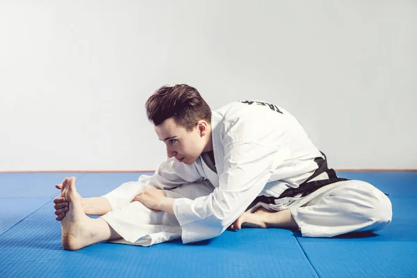 Chica en traje de karate kimono en estudio en fondo gris. La niña muestra judo o karate stans en uniforme blanco con cinturón negro. Deporte individual de arte marcial. retrato corporal — Foto de Stock