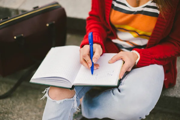 Menina bonita sentada na rua com um caderno e caneta na mão, fazendo notas e descansa . — Fotografia de Stock
