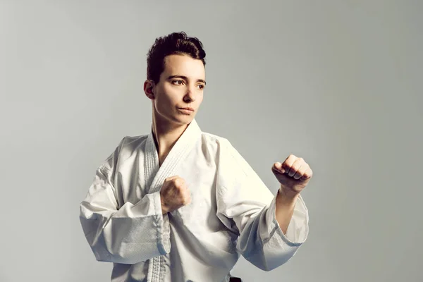 Chica en traje de karate kimono en estudio en fondo gris. La niña muestra judo o karate stans en uniforme blanco con cinturón negro. Deporte individual de arte marcial. retrato corporal — Foto de Stock