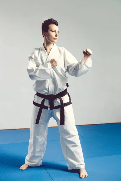 Girl in karate suit kimono in studio at grey background. Female child shows judo or karate stans in white uniform with black belt. Individual martial art sport . body portrait — Stock Photo, Image