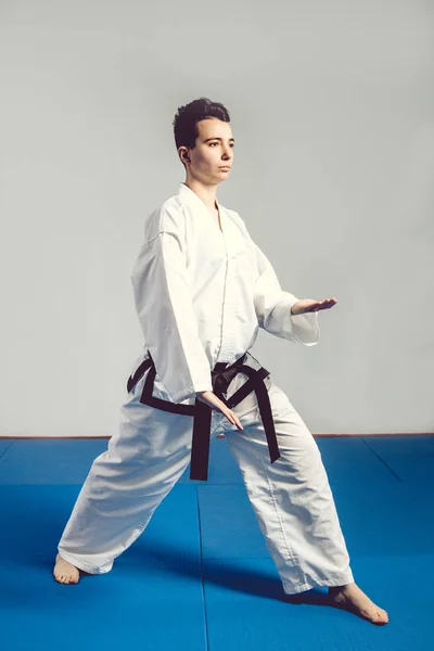 Dziewczyna w karate garnitur kimono w studio na szarym tle. Kobiece dziecko pokazuje judo i karate stans w biały uniform z czarnym pasem. Pojedyncze sztuki walki sport. portret ciała — Zdjęcie stockowe