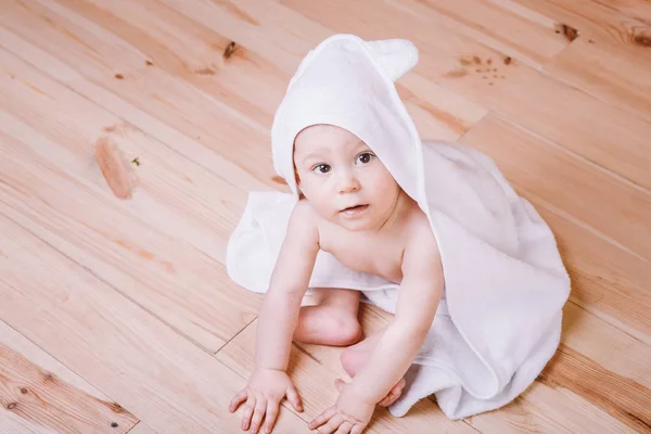 Αγοράκι με καστανά μάτια είναι πέντε μηνών τυλιγμένο σε μια λευκή πετσέτα με τα αυτιά σε φόντο ξύλινη . — Φωτογραφία Αρχείου