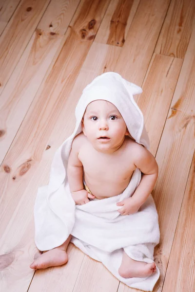 Bebé niño con ojos marrones es de cinco meses de edad envuelto en una toalla blanca con orejas sobre fondo de madera  . — Foto de Stock