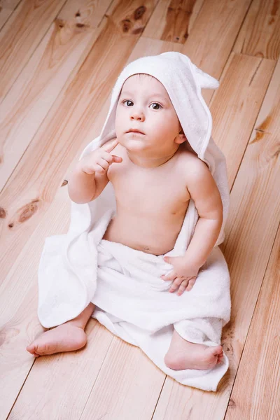 Bebé niño con ojos marrones es de cinco meses de edad envuelto en una toalla blanca con orejas sobre fondo de madera  . — Foto de Stock
