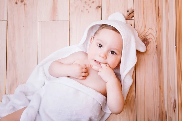 Menino com olhos castanhos tem cinco meses de idade envolto em uma toalha branca com orelhas no fundo de madeira  . — Fotografia de Stock