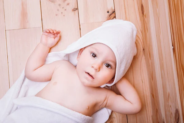 Junge mit braunen Augen ist fünf Monate alt, eingewickelt in ein weißes Handtuch mit Ohren auf hölzernem Hintergrund . — Stockfoto