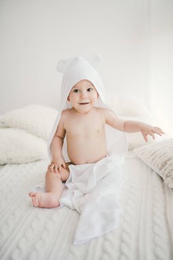 güzel yeni doğan bebek boy gülümseyerek kaplı beyaz bambu havlu ile oyunculuk ile kulaklar. Bir beyaz örgü, yün ekose parlak iç üzerinde oturuyor. Sağ penceresinde