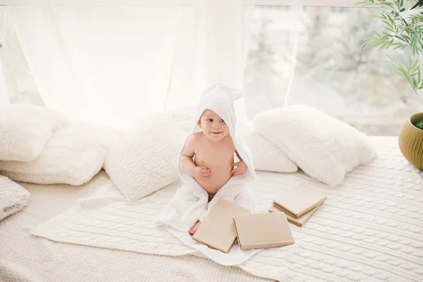 El chiquitín en la toalla blanca de bambú con las orejas sentadas en la manta tejida con los libros en el fondo de la ventana grande . — Foto de Stock