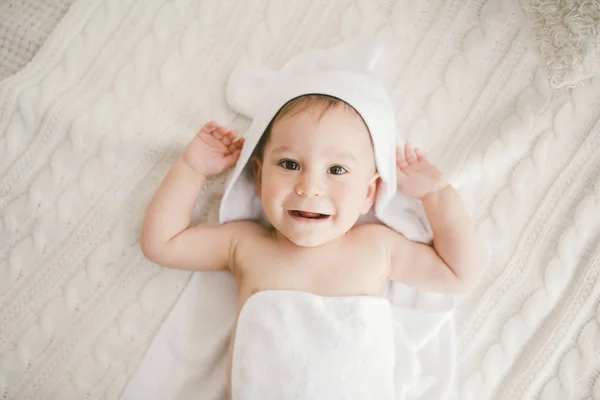Όμορφο χαμόγελο νεογέννητο αγοράκι που καλύπτεται με λευκή μπαμπού πετσέτα με διασκέδαση αυτιά. Κάθεται σε μια λευκή δεμένη, μάλλινο καρό φωτεινούς εσωτερικούς χώρους. Η δεξιά από το παράθυρο — Φωτογραφία Αρχείου
