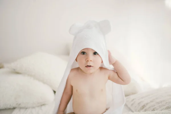 Όμορφο χαμόγελο νεογέννητο αγοράκι που καλύπτεται με λευκή μπαμπού πετσέτα με διασκέδαση αυτιά. Κάθεται σε μια λευκή δεμένη, μάλλινο καρό φωτεινούς εσωτερικούς χώρους. Η δεξιά από το παράθυρο — Φωτογραφία Αρχείου
