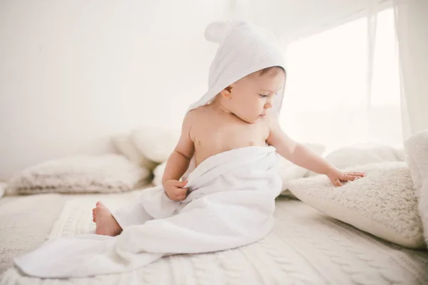 Mooie lachende pasgeboren babyjongen bedekt met witte bamboe handdoek met leuke oren. Zittend op een witte gebreide, wollen plaid helder interieur. De vlucht vanuit het venster — Stockfoto