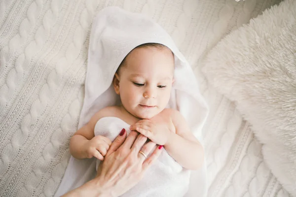 Lindo menino recém-nascido sorridente coberto com toalha de bambu branco com orelhas divertidas. encontra-se em um tricô branco, lã xadrez interior brilhante. A mão da mãe está na criança. A luz natural — Fotografia de Stock