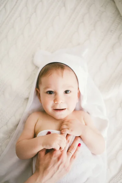 Lindo menino recém-nascido sorridente coberto com toalha de bambu branco com orelhas divertidas. encontra-se em um tricô branco, lã xadrez interior brilhante. A mão da mãe está na criança. A luz natural — Fotografia de Stock