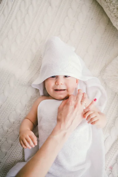 Beautiful smiling newborn baby boy covered with white bamboo towel with fun ears. lies on a white knit, wool plaid bright interior. The mom's hand is on the child. The natural light — Stock Photo, Image