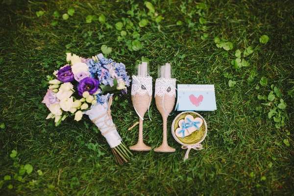 Zwei Gläser mit Blumen, eine Flasche Champagner und Eheringe auf dem Rasen. Hochzeitsaccessoires — Stockfoto