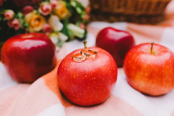 Red apples and wedding rings on a plaid blanket near the basket — Stock Photo, Image