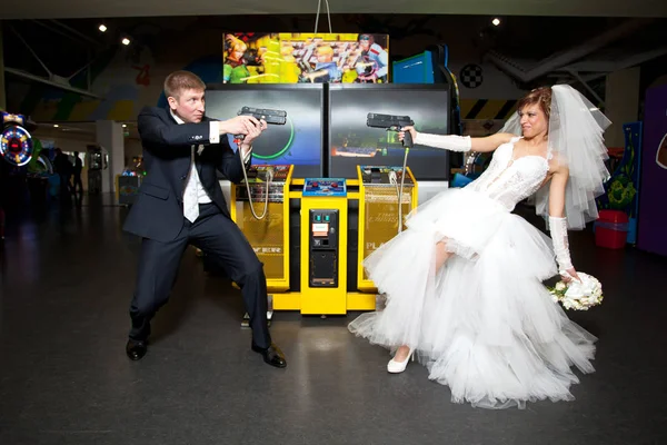 Casal amoroso em suas roupas de casamento jogando videogames no shopping. Armas nas mãos — Fotografia de Stock