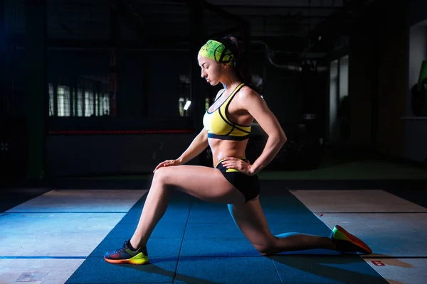 Hermoso, fuerte, delgado, en buena forma física en el gimnasio haciendo ejercicios. Vestido con pantalones cortos y camiseta verde, en la venda de la cabeza . — Foto de Stock