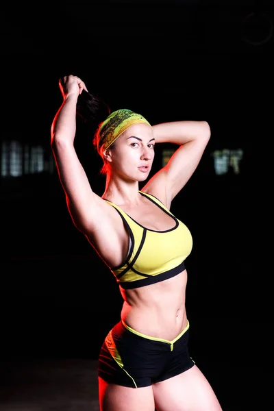Belle fille athlétique debout avec les mains levées dans la salle de gym. Vêtu d'un short et d'un t-shirt avec un bandage sur la tête. Concept sportif . — Photo