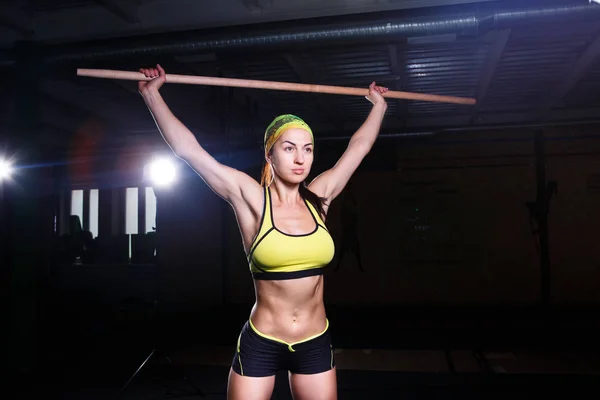 Joven hermosa chica está haciendo ejercicio en el gimnasio. Sostiene un palo sobre su cabeza para trinorvki músculos de las piernas. Concepto deportivo — Foto de Stock