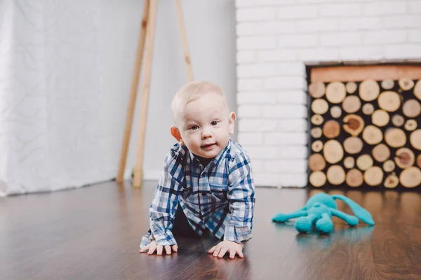 Ένα μικρό παιδί, ένα αγόρι που κάθεται σε ένα ξύλινο πάτωμα σε μια φωτεινή αίθουσα για ένα χρόνο. Ντυμένος με μπλε τζιν και ένα μπλουζάκι. Οικογένειας έννοια — Φωτογραφία Αρχείου