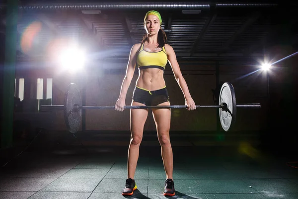 Una hermosa joven en el gimnasio entrena los músculos de las piernas y la espalda, ejercicios de deaet deadlift, se sienta con peso, sostiene la barra en sus manos — Foto de Stock