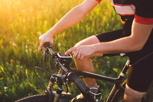 Młoda brunetka faceta na rowerze górskim używa komputer rowerowy, Nawigator w pole zachód słońca dnia — Zdjęcie stockowe