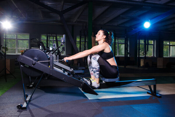 Молодая сильная девушка делает упражнения на гребном тренажере. Для тренировки сердечных мышц, назад. Спортивные концепции
