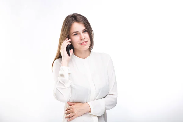 Hermosa joven con una camisa blanca sobre fondo blanco aislado hablando en un teléfono móvil. Retrato de sonrisas en la cintura —  Fotos de Stock