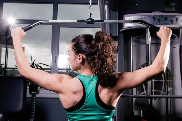 Una vista posterior de una chica entrenada haciendo ejercicios. Entrenamiento para los músculos de espalda — Foto de Stock