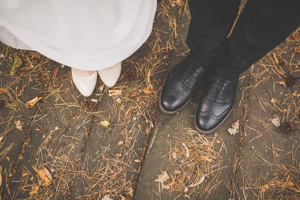 Ноги жениха и невесты: черные туфли, туфли на белых каблуках, детали свадебного платья — стоковое фото