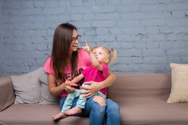 Anne ve bebek oynamak ve eğlenmek kanepede odasında. Onlar parlak giysilerle giyindin. Çekici, şık ve genç ailesi