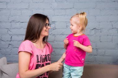 Anne ve bebek oynamak ve eğlenmek kanepede odasında. Onlar parlak giysilerle giyindin. Çekici, şık ve genç ailesi
