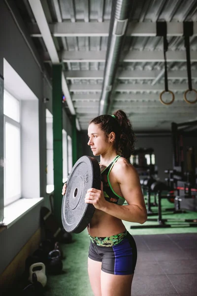Krásný, svalnatý, sportovní dívka dělá cvičení na svaly na rukou a zádech. Drží hmotnost na pozadí v tělocvičně — Stock fotografie