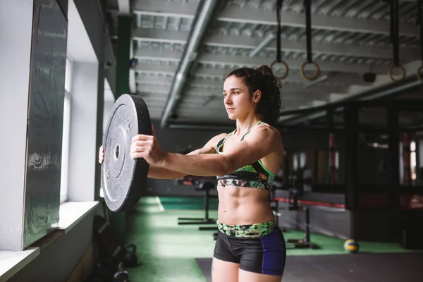 En vacker, muskulös, atletisk flicka gör övningar på musklerna i händer och rygg. Har vikt i bakgrunden på gymmet — Stockfoto