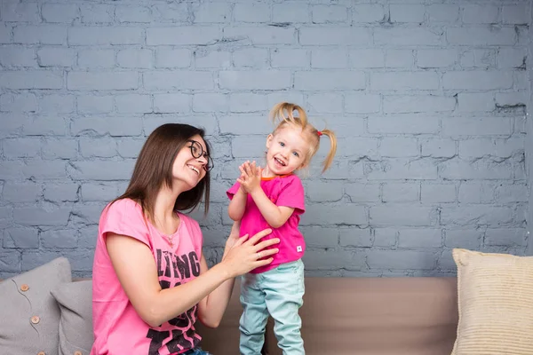 Anne ve bebek oynamak ve eğlenmek kanepede odasında. Onlar parlak giysilerle giyindin. Çekici, şık ve genç ailesi
