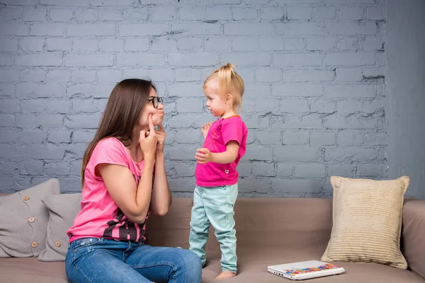 Anne ve bebek oynamak ve eğlenmek kanepede odasında. Onlar parlak giysilerle giyindin. Çekici, şık ve genç ailesi