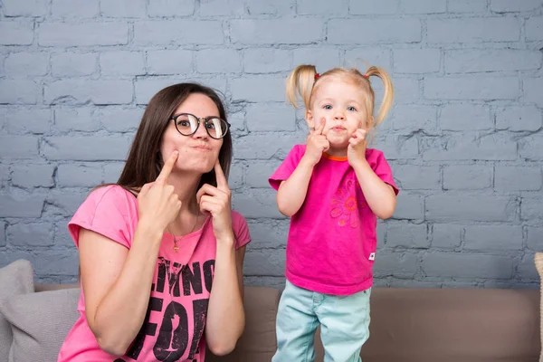 Maman et bébé jouent et s'amusent dans la chambre sur le canapé. Ils sont vêtus de vêtements lumineux. Jolie, élégante et jeune famille — Photo