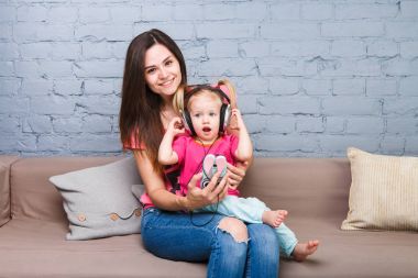 Anne ve kızı büyük kulaklık onların başının üstüne koy kanepede oturan dinleyin. Telefon tutar.