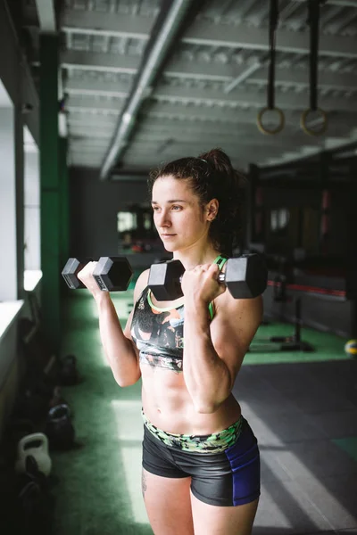 Attraktiv vältränad kvinna som funkar med hantlar som en konceptuell i gymmet fitness — Stockfoto