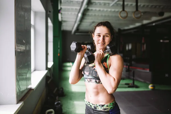 Mulher ajuste atraente trabalha com halteres como um conceito de fitness no ginásio — Fotografia de Stock