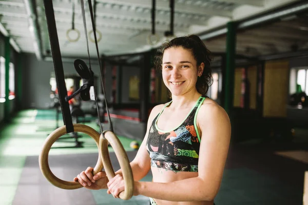 Hermosa chica haciendo un ejercicio en los anillos del gimnasio en el gimnasio. Feliz y sonriente . — Foto de Stock