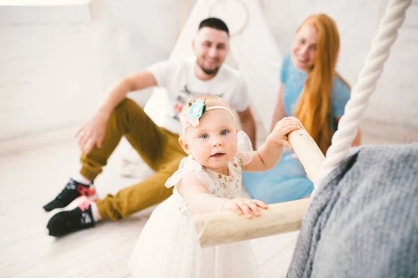 En lycklig familj på tre. Mamma, Pappa, barn ett år gammal flicka i klänning spel, skratta, Le i ljusa rum. Soligt — Stockfoto