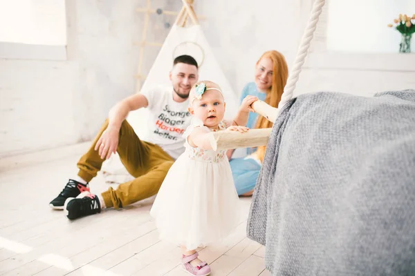 Een gelukkig gezin van drie. Vader, moeder, kind één jaar oud meisje in jurk spelen, lachen, glimlachen in lichte kamer. Zonnige — Stockfoto