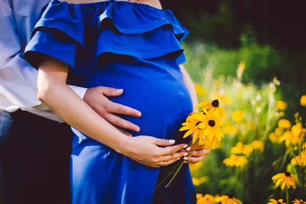 Father and pregnant mother holding hands together with yellow flowers on a green meadow. — Stock Photo, Image