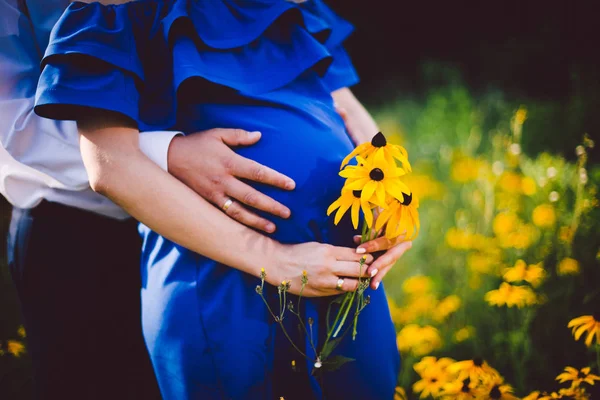 아버지와 임신한 어머니 녹색 초원에 노란색 꽃과 함께 손을 잡고. — 스톡 사진