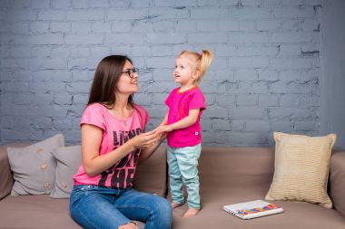 Anne ve bebek oynamak ve eğlenmek kanepede odasında. Onlar parlak giysilerle giyindin. Geri kalan bir çekici, şık ve genç ailesi