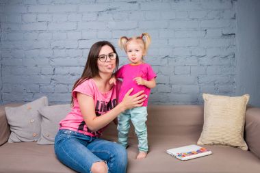Anne ve bebek oynamak ve eğlenmek kanepede odasında. Onlar parlak giysilerle giyindin. Geri kalan bir çekici, şık ve genç ailesi