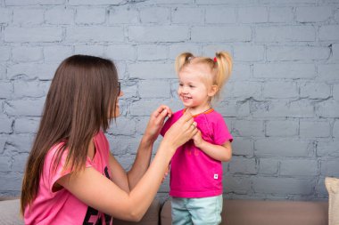 Anne ve bebek oynamak ve eğlenmek kanepede odasında. Onlar parlak giysilerle giyindin. Çekici, şık ve genç ailesi